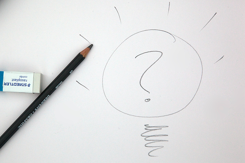 A question mark inside a lightbulb drawn in pencil on a white sheet of paper. The pencil and an eraser are laying next to the drawing.