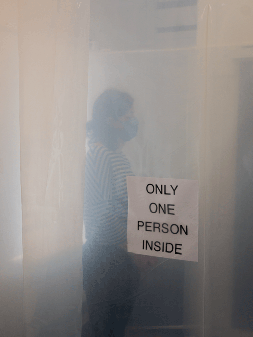 A person stood behind an opaque sheet with and 'Only One Person Inside' sign by artist Rachel Rosen