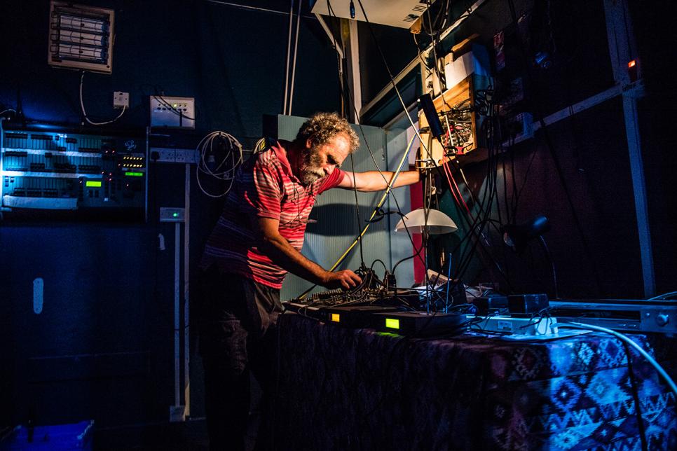 Older man turns dials on sound desk backstage.