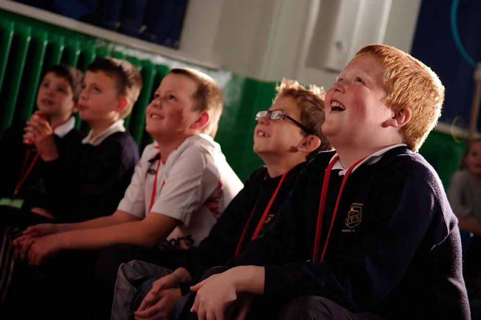 Four young boys sit down and look at a performance