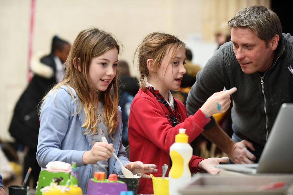 A male teacher helps two young girls with a craft project