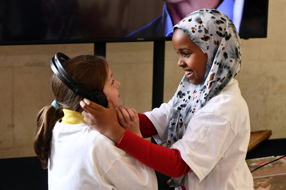 One smiling girl holds headphones over another girl's ears