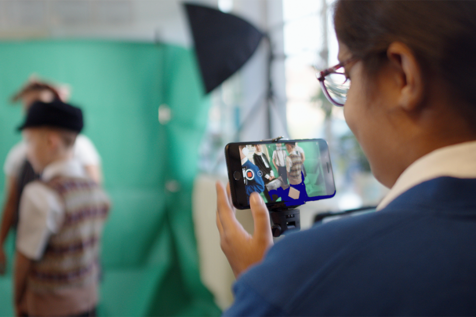Child holds iphone to film a green screen with other children in front of it