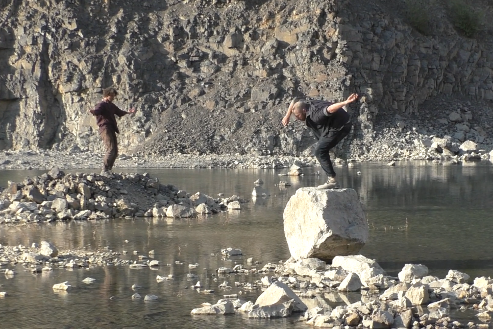 Dancers are standing on large rocks placed in a quarry with water surrounding them