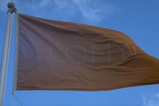 An orange flag waving in the wind with 'Llonydd' written on it