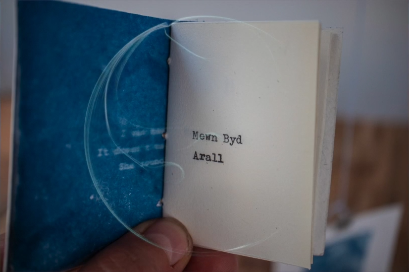 A small book with the words 'Mewn Byd Arall' or 'In Another World' written in it.