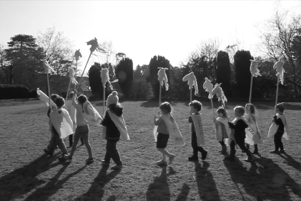 A group of children walk across a field carrying flags