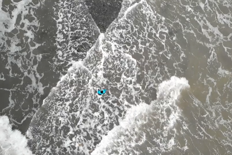 A person in a bright blue top is standing in the middle of a grey sea