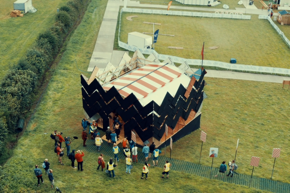 Audiences gather around an artistic structure in a field