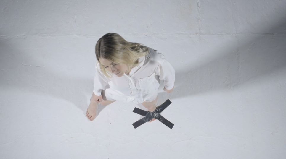 Looking downwards onto a woman in a white shirt with her foot taped to the ground.