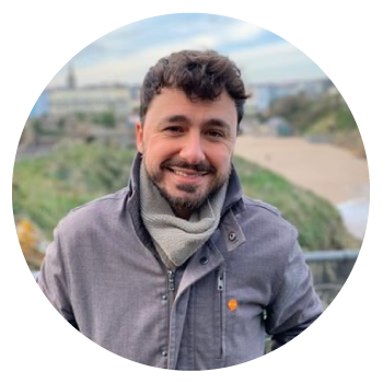 Nick Yeo wearing a grey jacket and scarf in front of a green landscape.