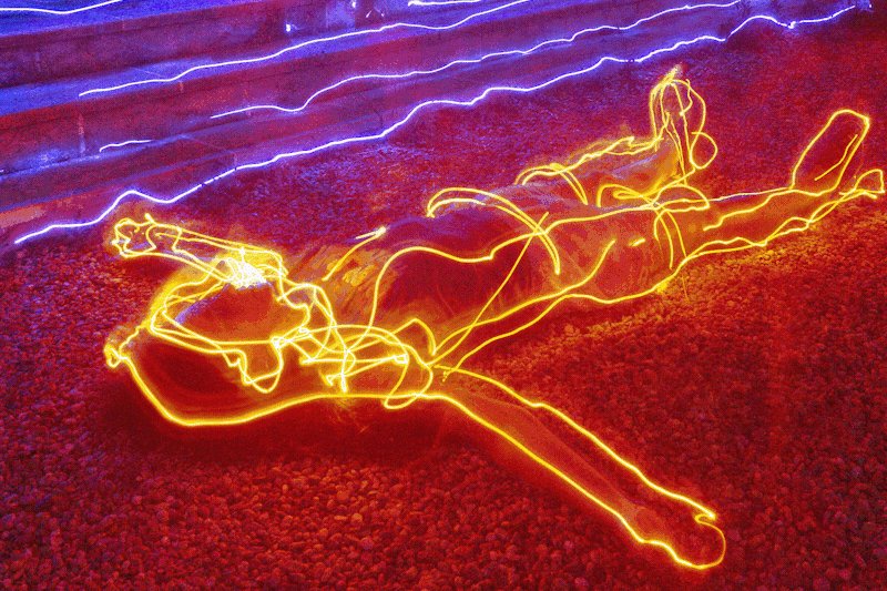 A person lies on the floor in the foreground, with orange light outlining their body, and blue light in strips in the background