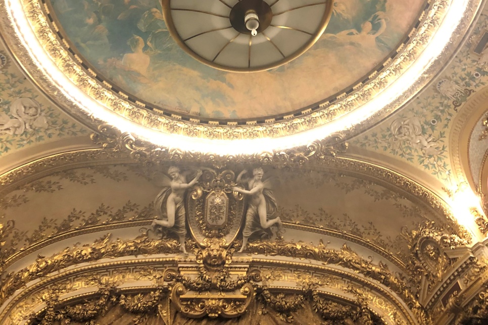 The grand ceiling of Opera Comique Paris with sky-like ceiling art surrounded by a circle of white lights