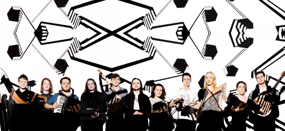 Group of musicians stood in a line, in front of a black and white abstract background.