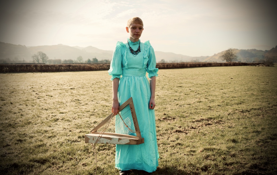 Woman in a mint green long dress holding a harp, in a Wintery field.