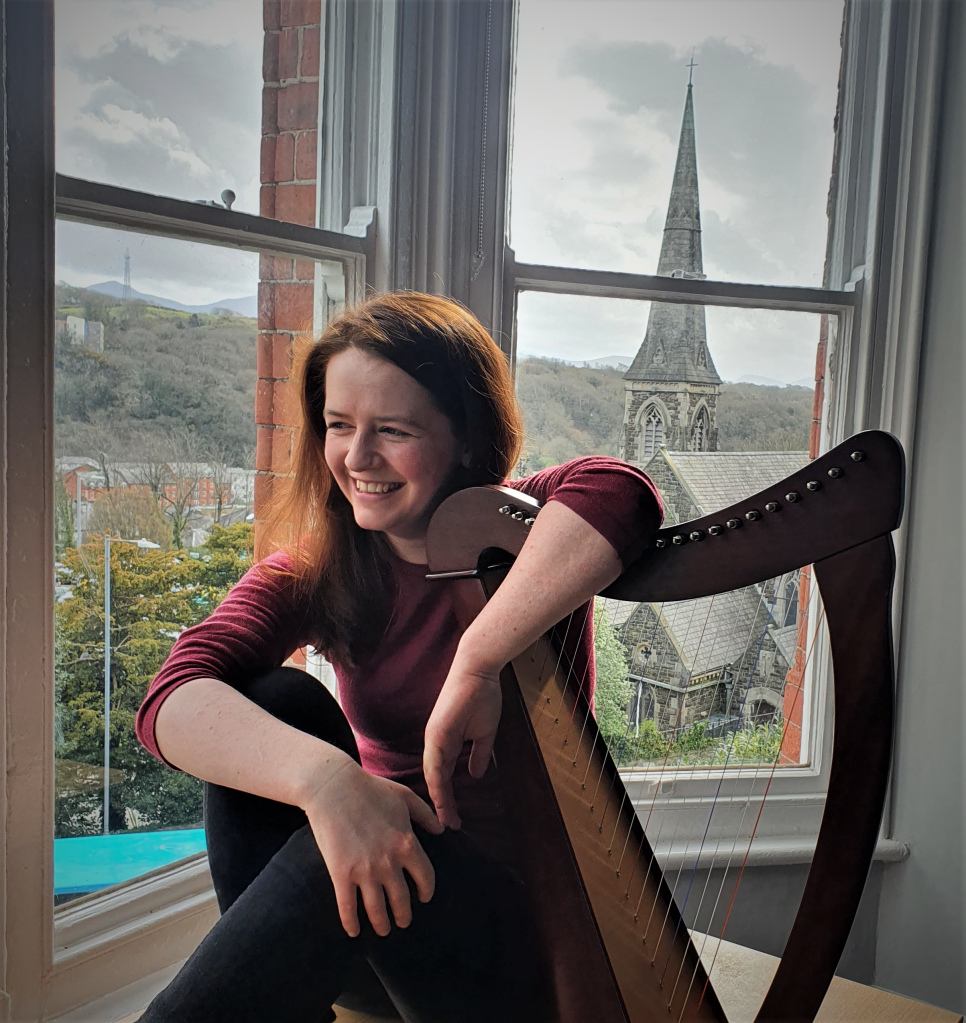 Women smiling in front of window, clasping a harp.