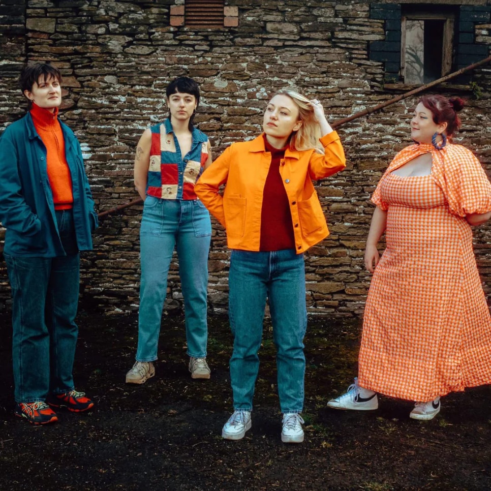  4 women in colourful clothes stood outside a stone-walled building