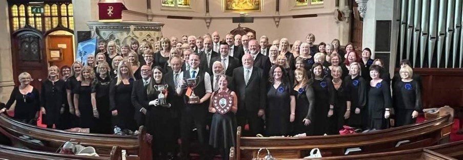Large choir group, smiling, holding awards in a church setting.