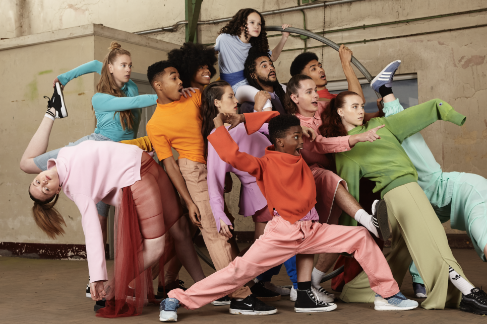 Large group of young dancers in brightly coloured clothing, leaning backwards