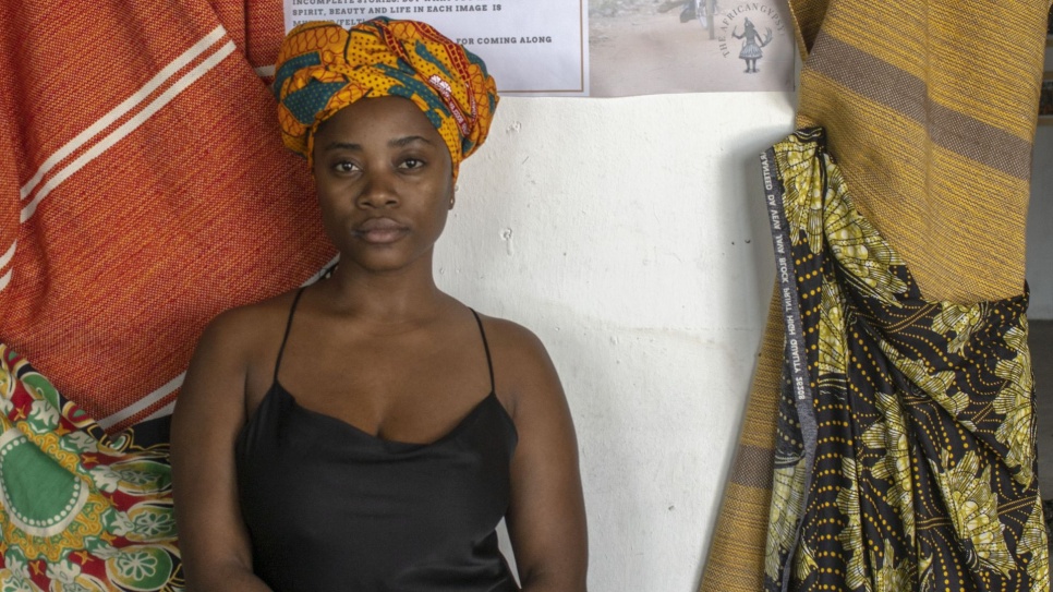 Chembo Liandisha stood in front of trafidional African fabrics wearing a black dress and traditional African headwear