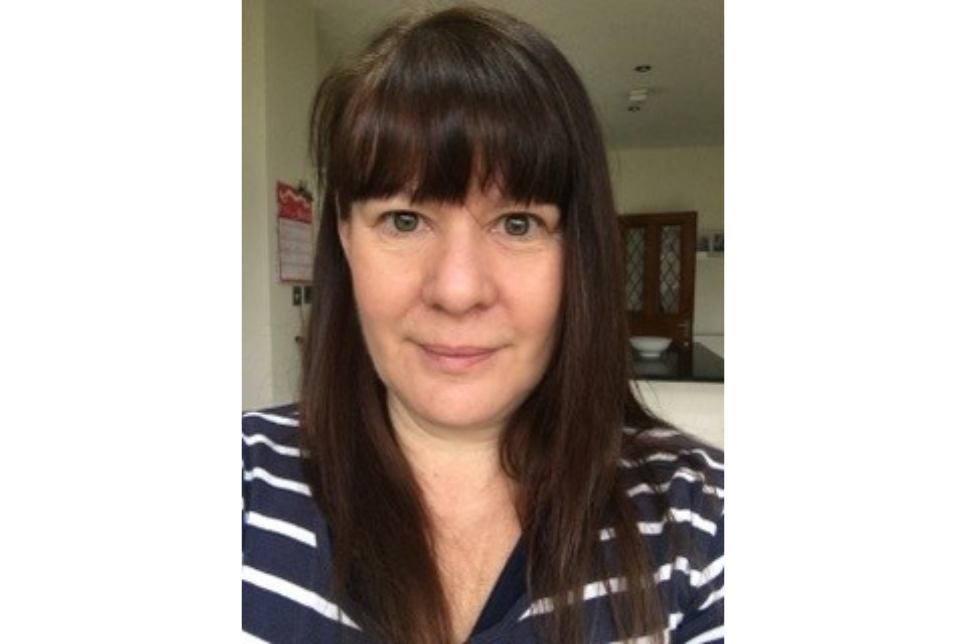 Portrait of Karen Pimbley with shoulder-length brown hair, wearing a striped shirt, taken indoors.