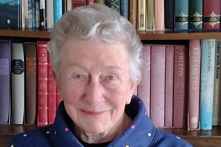 Woman sitting in front of a bookshelf in a blue patterned top 