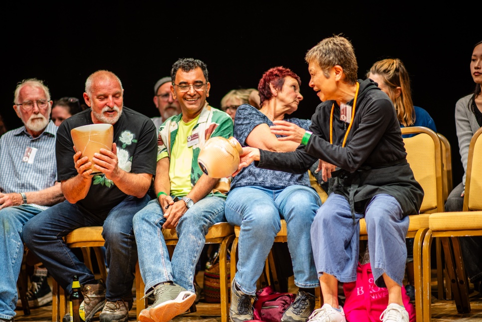 People sat on chairs, smiling, sharing pottery pieces