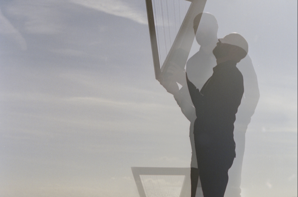 Double exposure image of a man holding a harp on a beach